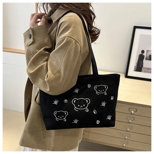 Close-up of black canvas tote bag featuring white cartoon bear embroidery detail