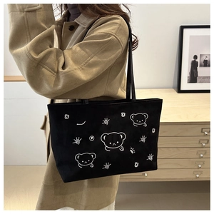 Detail showing high-capacity black canvas tote bag with artistic cartoon bear illustration