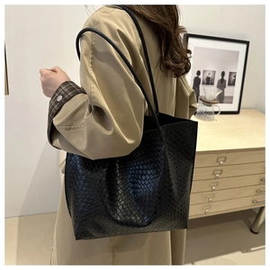 Close-up of black textured leather tote bag with long straps worn on a trench coat