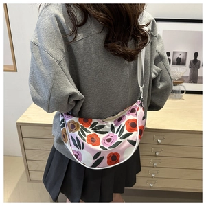 Detail of floral half-moon crossbody bag with wide white strap worn on shoulder
