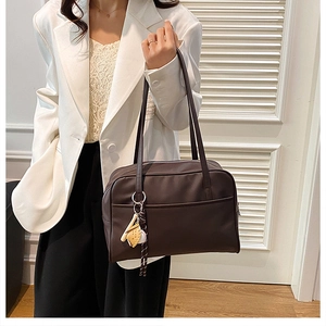 Detail of dark brown leather tote bag with unique baseball glove charm on shoulder strap