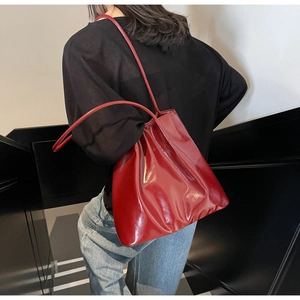 Detailed view of glossy red patent leather tote bag styled on model in dark interior