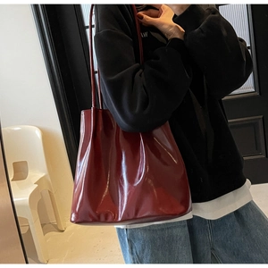 Deep burgundy glossy faux leather tote bag being worn by a model in a casual setting