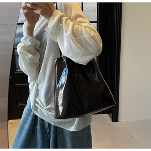 Close-up of a large dark brown glossy patent leather tote bag worn by a model