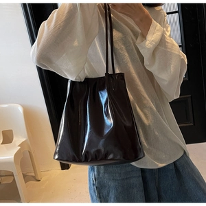 Detail showing the glossy finish and slim shoulder strap of the brown patent leather tote bag
