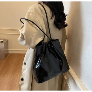 Glossy black faux leather tote bag worn by a model in a beige trench coat for a minimalist look