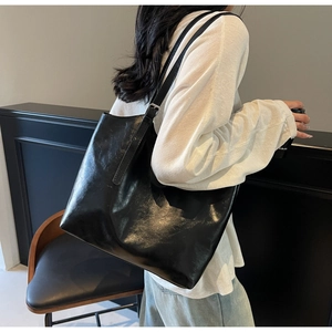Macro detail of glossy black oil wax leather tote bag with silver metal buckle and texture