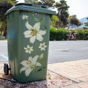 Outdoor green trash can with elegant white lily floral decals on a gravel path