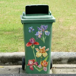 Detail of green mobile waste bin featuring colorful iris floral stickers and rolling wheels