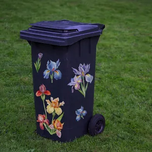 Detail view of decorative iris flower stickers on a large black outdoor trash bin with wheels