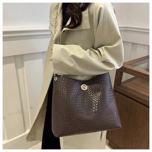 Détail du sac à bandoulière tressé marron foncé avec chaîne dorée sur manteau beige