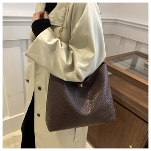 Détail d'un sac à bandoulière marron foncé tressé avec chaîne dorée et fermoir pivotant