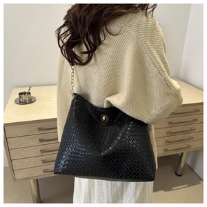 Détail d'un sac bandoulière noir tressé avec bandoulière en chaîne dorée et fermoir pivotant