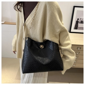 Détail d'un sac à bandoulière tressé noir avec chaîne dorée et fermoir rotatif en métal