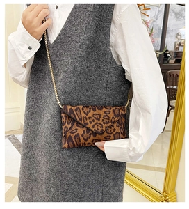 Close-up of leopard print envelope clutch bag with gold chain strap worn cross-body