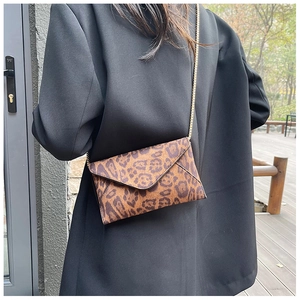 Close-up of leopard print envelope clutch with gold chain strap worn by a model