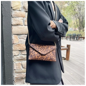 Leopard print envelope crossbody bag with gold chain strap styled on a black blazer