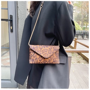 Close-up of leopard print envelope clutch bag with gold chain strap on a model