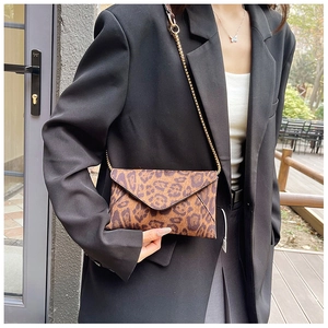 Detail of a leopard print envelope bag with a fine gold chain strap in an outdoor setting