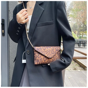 Detail of leopard print envelope clutch featuring a gold chain strap worn with a black blazer