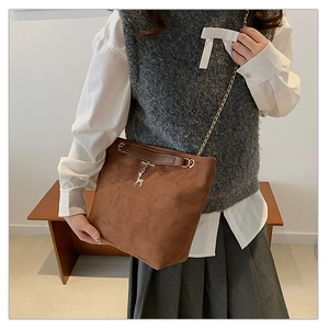 Detail of brown suede tote bag featuring a metallic chain strap and a deer charm accessory
