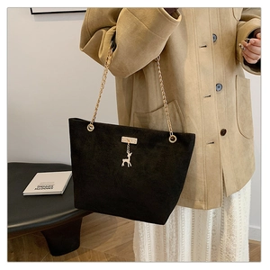 Detail of black suede tote bag with golden deer pendant and elegant chain strap