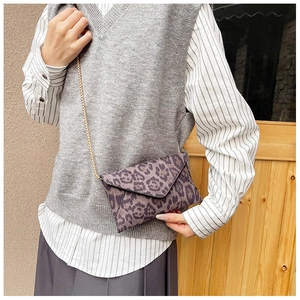 Detail of a stylish leopard print envelope bag with a thin gold chain strap on a model