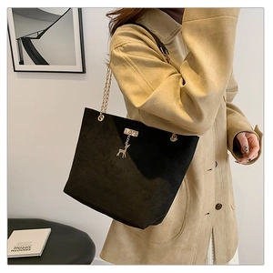 Detail of vintage black suede tote with gold chain strap and deer pendant on model