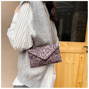 Leopard print envelope bag with gold chain strap worn by model in an urban setting
