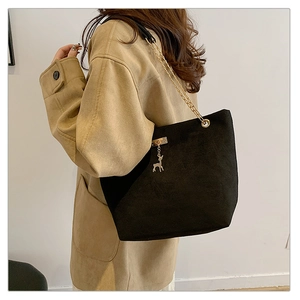 Detail of black suede tote bag with golden metal chain strap and deer pendant