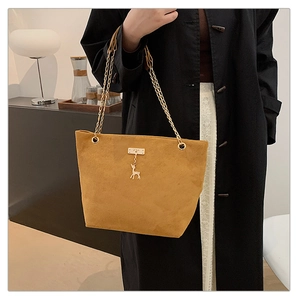 Detail of a ginger yellow suede handbag with a golden deer charm and chain straps