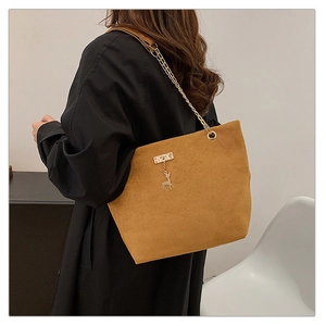 Detail of brown suede tote bag featuring a gold chain strap and decorative deer charm