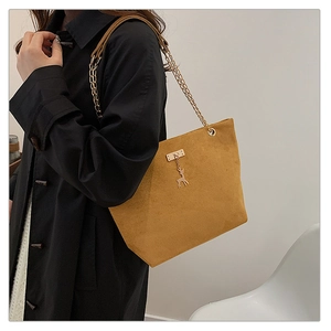 Detail of mustard yellow suede tote bag featuring a gold chain strap and deer pendant accessory