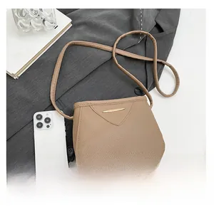 Détail du sac bandoulière en cuir kaki avec garniture dorée à côté d'un smartphone