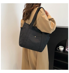 Detail shot of a large black canvas tote bag with a snap pocket on model's shoulder