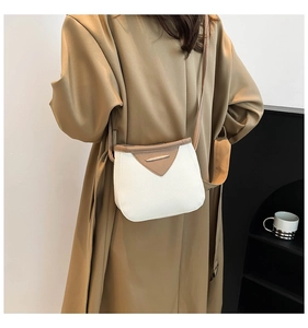 Vue détaillée d'un sac bandoulière blanc et marron porté sur un trench-coat kaki chic