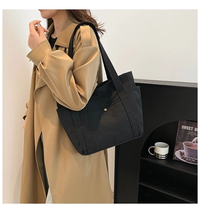 Detail of black canvas tote bag with side pockets and wide shoulder strap on a model
