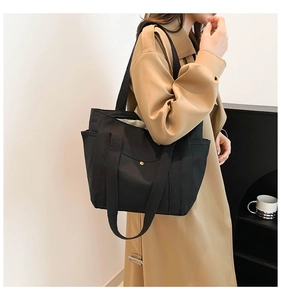 Detail view of large black canvas tote bag showing metal snap button pocket and wide strap