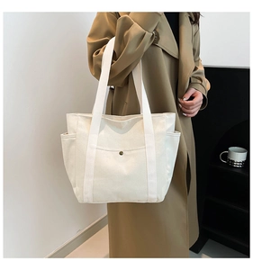 Detail view of large cream canvas tote bag with side pockets and metal snap button