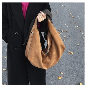 Detail of a brown suede Hobo tote bag with metal zipper and wide handle in autumn street scene