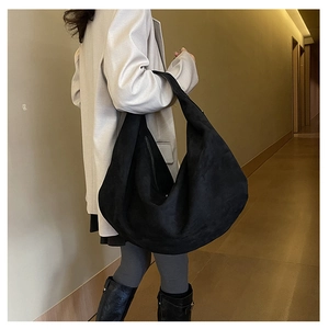 Large black suede hobo bag with draped silhouette and wide shoulder strap in daily use
