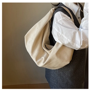 Side view of model wearing a large beige pleated tote bag with matte suede texture