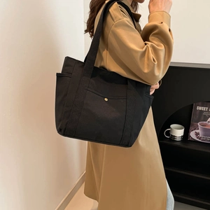 Large black canvas tote bag with metal snap pocket and shoulder strap for daily commuting