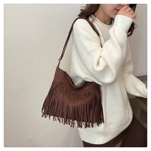 Detail of dark brown faux suede shoulder bag with dense tassels on a white knit sweater