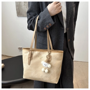 Detail of beige tote bag with brown leather strap and plush charm on grey blazer