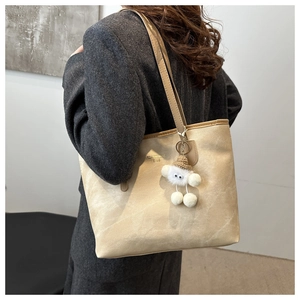 Close-up of beige faux leather tote bag with plush charm and gold embossed lettering