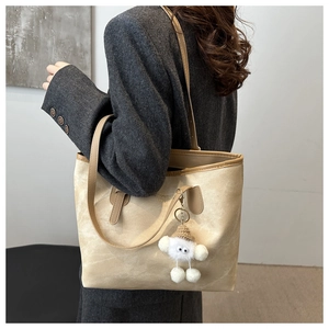 Detail of beige tote bag with a white plush knit charm pendant and shoulder strap