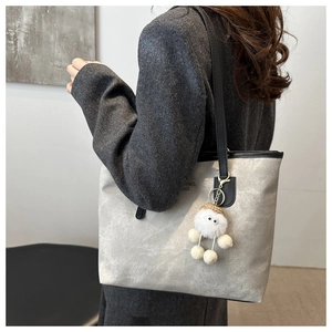 Detailed view of grey tote bag with plush charm on a model in professional grey suit