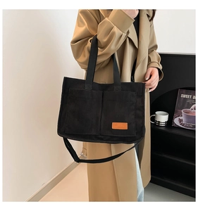 Detail of black corduroy tote bag with orange fashion label and front pockets worn with a coat