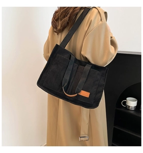 Detail of black corduroy tote bag featuring leather 'FASHION' label and woven shoulder strap
